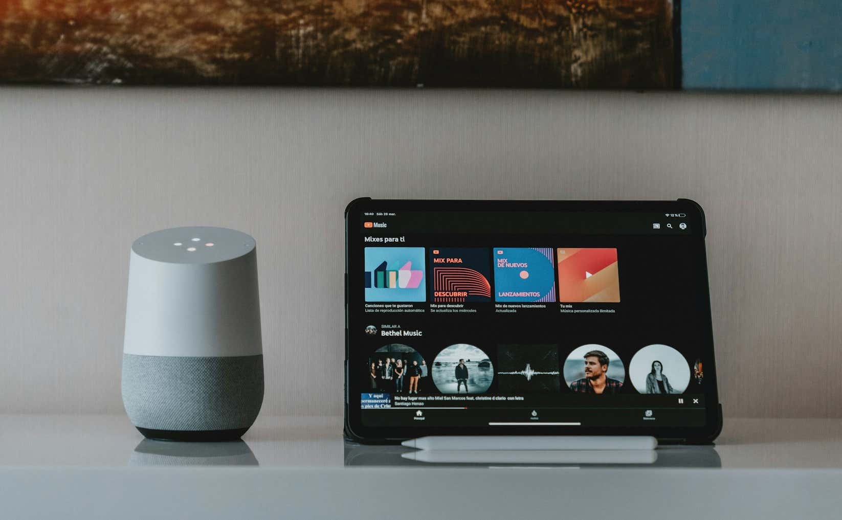 A Google Home Speaker sits next to an iPad with YouTube Music open on the screen